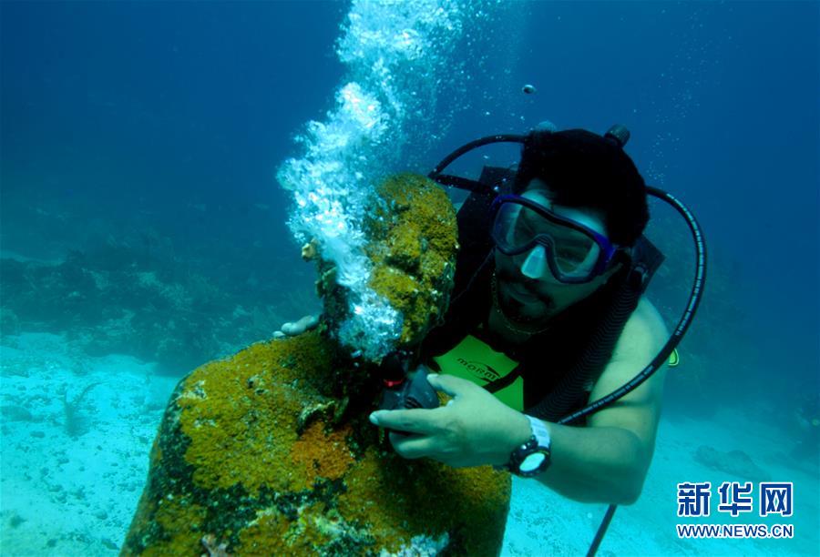 水下呼吸 9月29日，在墨西哥坎昆，一名游客在加勒比海潜水时给海底的雕塑戴上呼吸器。 记者 淡航/摄